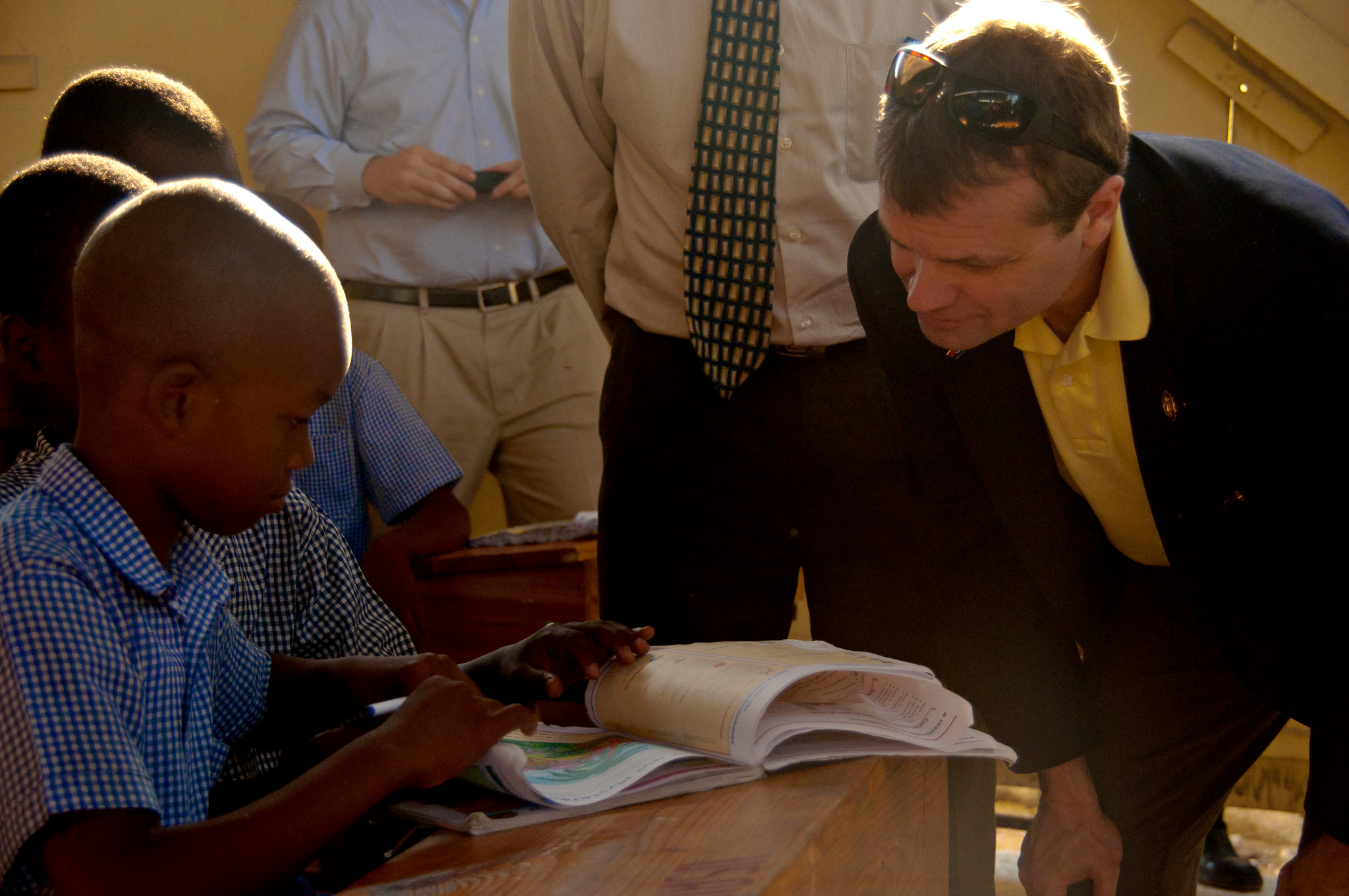 USAID worker in suit speaking to an African child reading a book.