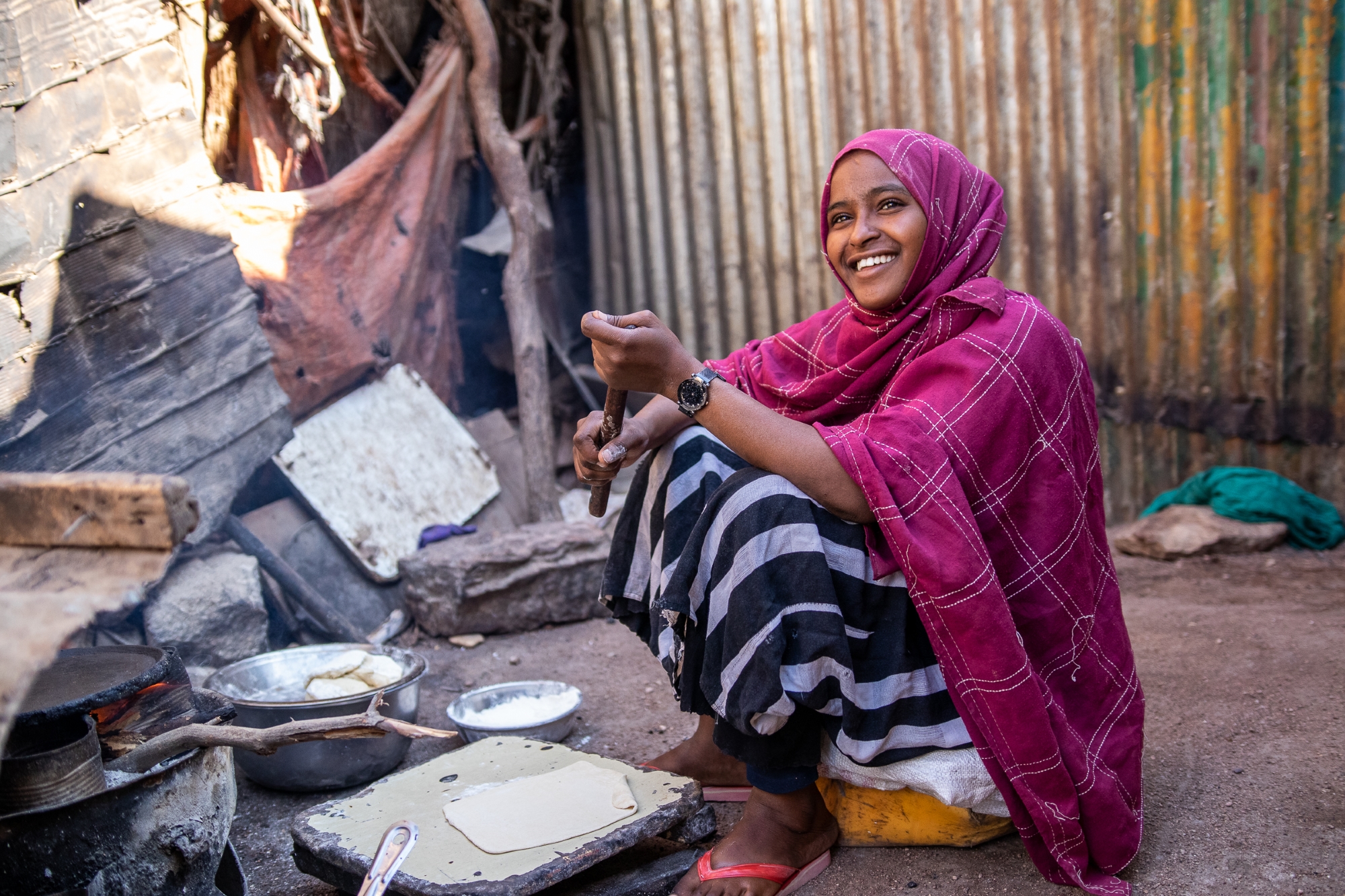 Saynab, a 14-year-old girl, has impacted by the drought in Somalia and sells chapatis to support her family. She smiles as she cooks chapatis.