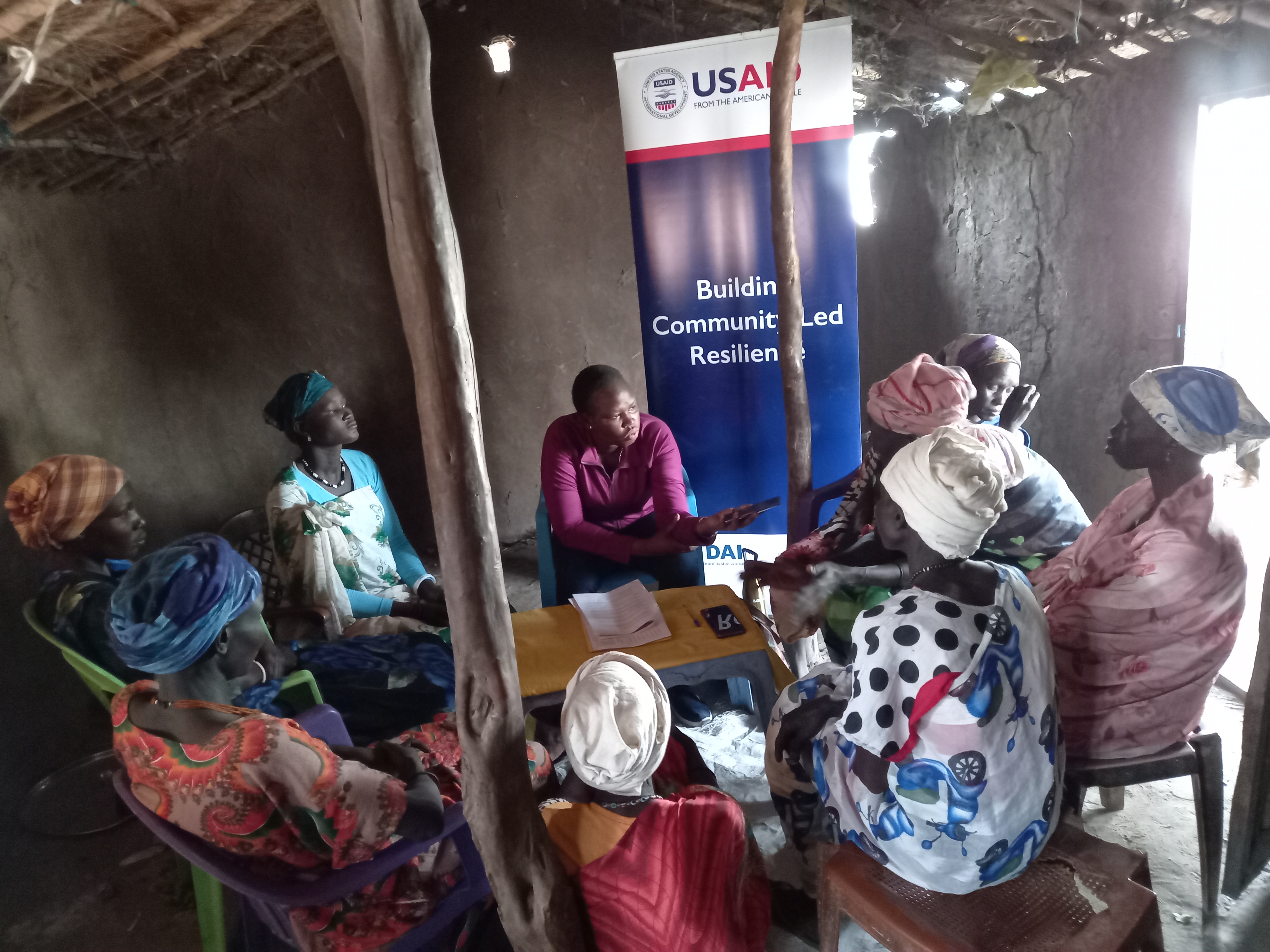 group of South Sudan community members sitting in a circle in front of a USAID banner