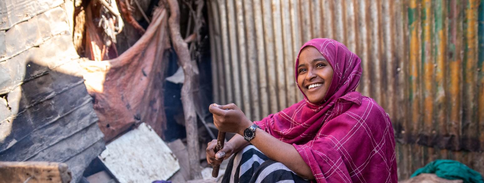 Saynab, a 14-year-old girl, has impacted by the drought in Somalia and sells chapatis to support her family. She smiles as she cooks chapatis.